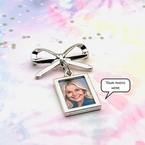 May include: Silver bow brooch with a small silver frame attached. The frame has a photo of a woman inside. The text "YOUR PHOTO HERE" is in a speech bubble.
