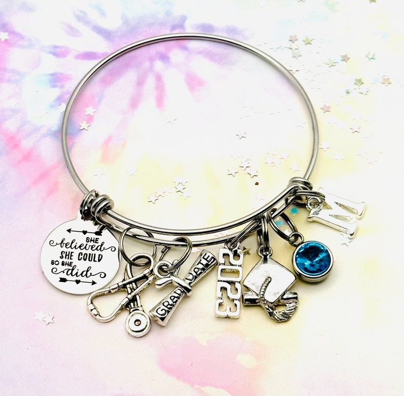 A stainless steel nurse graduate charm bracelet that is available in 3 sizes. This gift will arrive with the following charms, She believed she could so she did, stethoscope, diploma, 2023, grad cap, and your choice of initial and birthstone.