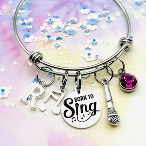 May include: A silver charm bracelet with a pink rhinestone charm, a microphone charm, a music note charm, and a charm that says "Born to Sing".