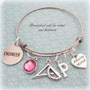 May include: A silver charm bracelet with charms that say "Engineer", "Amazing Woman", and "P". There is also a pink rhinestone charm and a charm that looks like a protractor and ruler.
