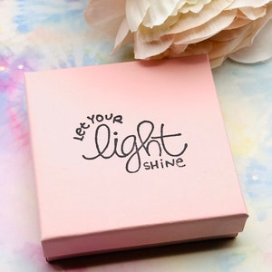 May include: A pink gift box with the words "Let your light shine" printed on the top in black lettering.