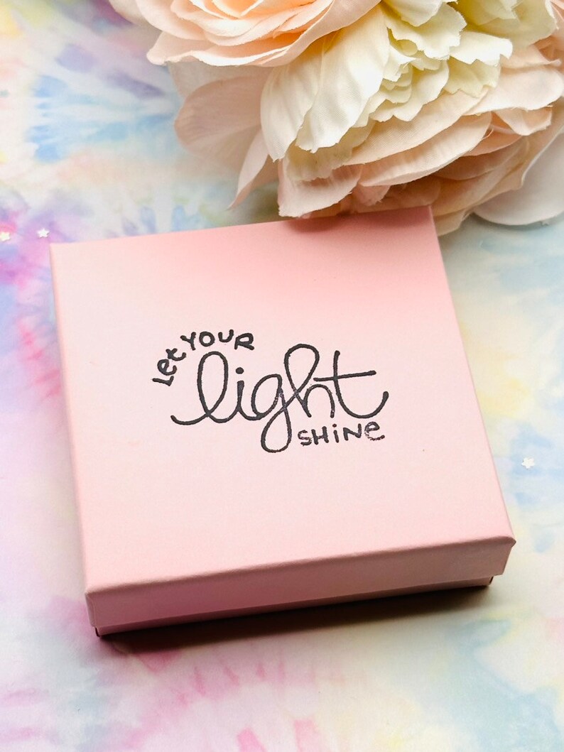 May include: A pink gift box with the words "Let your light shine" printed on the top in black lettering.