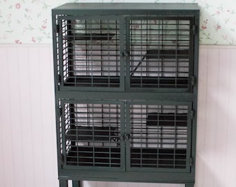 May include: A black metal cage with two levels and a bottom shelf. The cage has a door on each side of each level. The cage is sitting on a wooden floor. There are two black metal ladders on the floor in front of the cage.