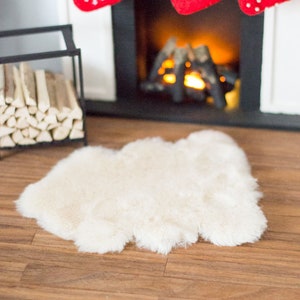 May include: A white faux fur rug sits in front of a fireplace with a glowing fire. Three red Christmas stockings hang from the mantel above the fireplace.
