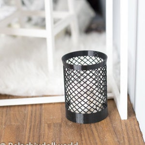 May include: A black wire mesh trash can with a white fuzzy rug in the background.