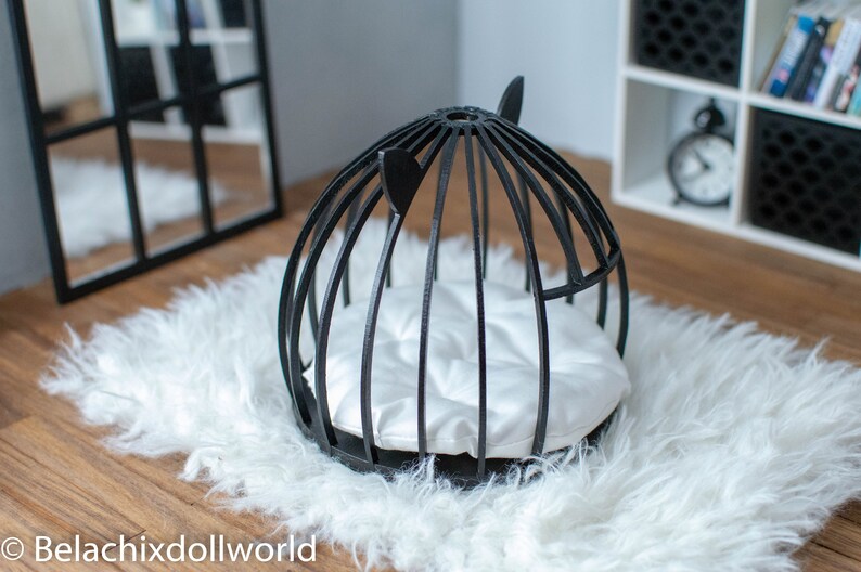 May include: Black wire cage pet bed with a white cushion. The bed is on a white fluffy rug.