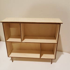 May include: A wooden shelf unit with five compartments, two on the top shelf and three on the bottom shelf. The shelf unit is made of light wood and has a natural finish.