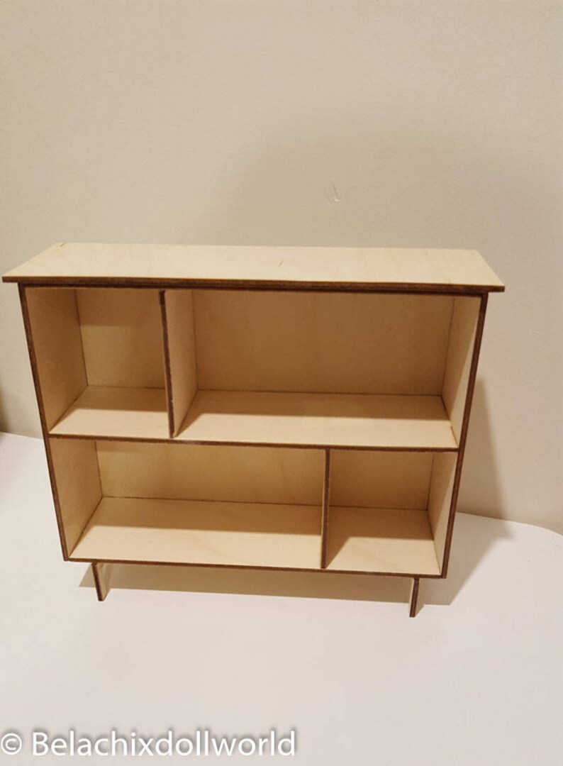 May include: A wooden shelf unit with five compartments, two on the top shelf and three on the bottom shelf. The shelf unit is made of light wood and has a natural finish.
