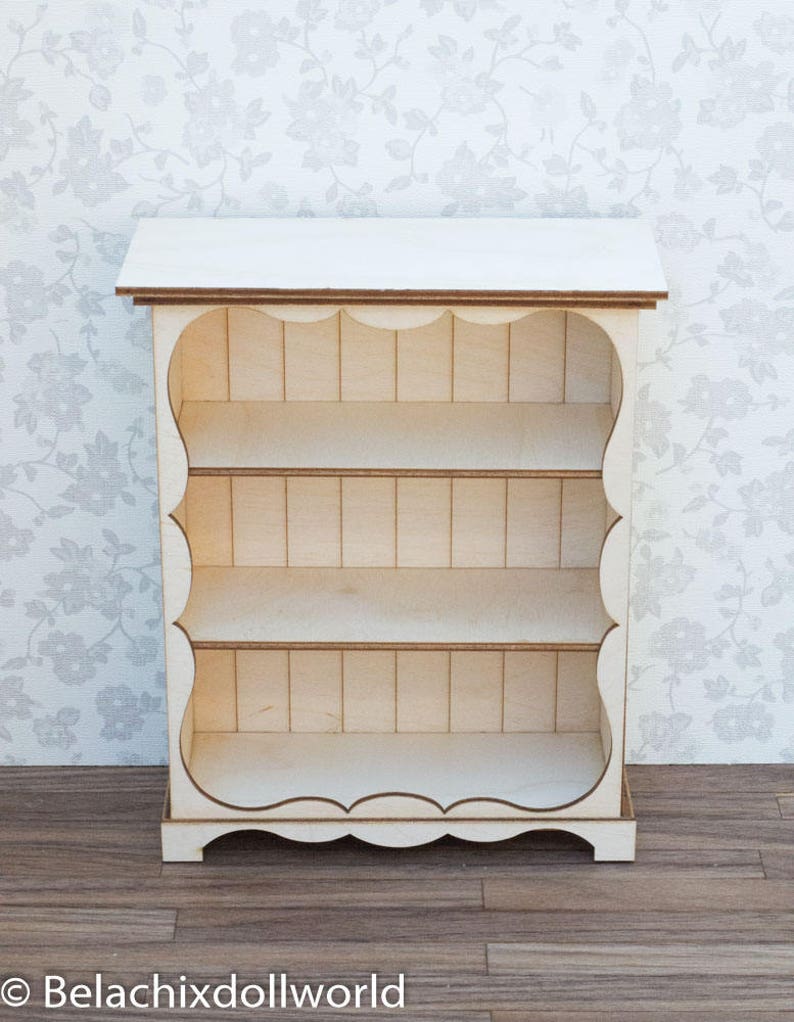 Pu&ograve; includere: Libreria in legno bianco con tre ripiani e un bordo a festoni. La libreria &egrave; in legno e ha una finitura bianca.