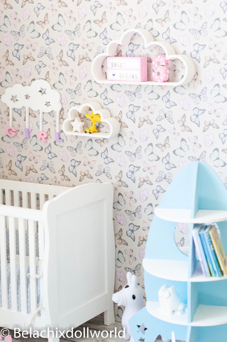 May include: A white crib with a white and gray patterned mattress, a white cloud-shaped shelf with a pink number 3 and a light box that says "Sweet Dreams", a white cloud-shaped shelf with a yellow giraffe toy, a blue rocket-shaped bookshelf with books, and a white rocking horse.