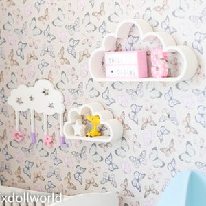 May include: White cloud-shaped shelves with a star design, mounted on a wall with a butterfly pattern wallpaper. The top shelf has a pink light box with the text "Sweet Dreams" and a pink number 3. The middle shelf has a small yellow toy giraffe. The bottom shelf has purple letters spelling "GIRL".