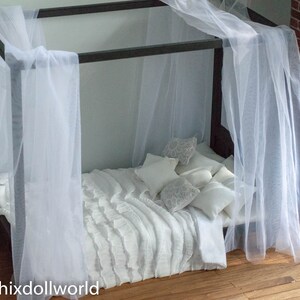 Puede incluir: Una cama con dosel blanco con un edred&oacute;n blanco con volantes y almohadas blancas. La cama est&aacute; hecha de madera oscura y tiene un dosel blanco de gasa.