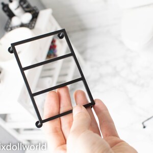 May include: Black metal shelf unit with three tiers. The shelf unit is designed for dollhouse decor.