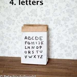 May include: A brown paper bag with the alphabet printed on it in black ink. The bag is sitting on a wooden floor with a floral wallpaper in the background. The text on the bag reads "4. letters".