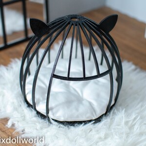 May include: Black cat-shaped bed for small pets, featuring a white cushion and a black wire frame. The bed is on a white fluffy rug.