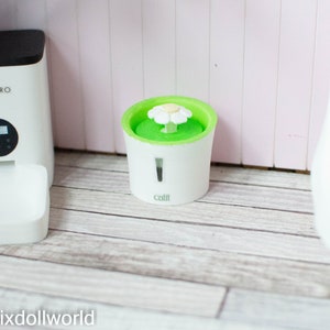 May include: White automatic pet feeder with a digital display and a white bowl. A white pet water fountain with a green top and a white flower on top. The fountain has the word "Catit" on the front.