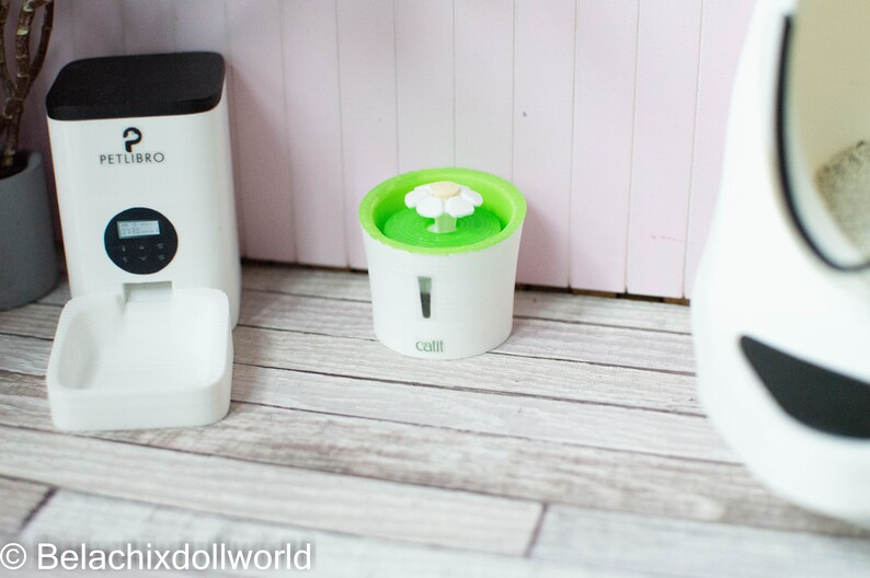 May include: White automatic pet feeder with a digital display and a white bowl. A white pet water fountain with a green top and a white flower on top. The fountain has the word "Catit" on the front.