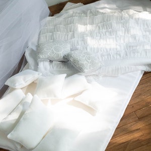 Puede incluir: Una cama blanca con un edred&oacute;n blanco con volantes y varias almohadas blancas. La cama est&aacute; sobre un suelo de madera.