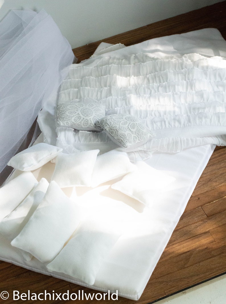 Puede incluir: Una cama blanca con un edred&oacute;n blanco con volantes y varias almohadas blancas. La cama est&aacute; sobre un suelo de madera.