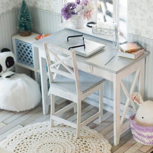 May include: A white wooden desk with a laptop, glasses, and books on top. A white wooden chair sits next to the desk. A white crocheted rug is on the floor. A white furry ottoman is in the background.