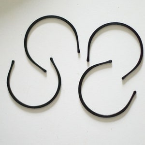 May include: Four black plastic headbands, each in a simple curved shape, arranged on a white surface.
