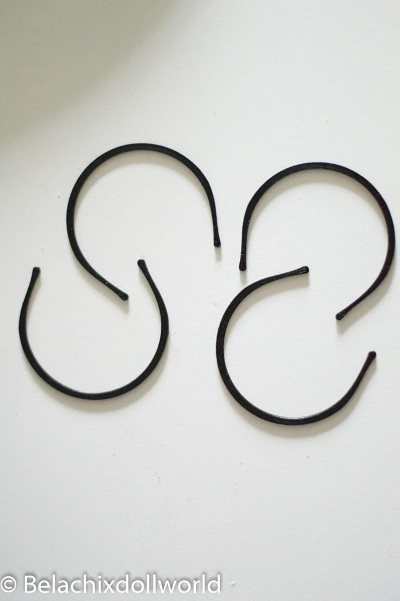 May include: Four black plastic headbands, each in a simple curved shape, arranged on a white surface.