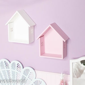 May include: Two small house-shaped shelves, one white and one pink, mounted on a lavender wall. The shelves are empty and have a simple design.