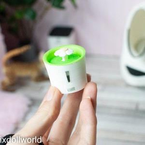 May include: A small, white and green cat water fountain with a white flower on top. The fountain is labeled "Catit".