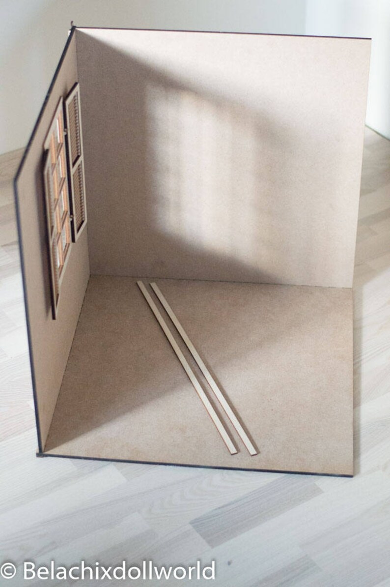 May include: A dollhouse room with beige walls and a wooden window. Two wooden strips are lying on the floor.