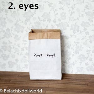 May include: A white paper bag with brown paper trim and two black eyes drawn on the front. The text "2. eyes" is written above the bag.