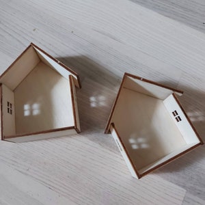 May include: Two unfinished wooden houses with cut-out windows. The houses are made of plywood and are sitting on a light wood surface.