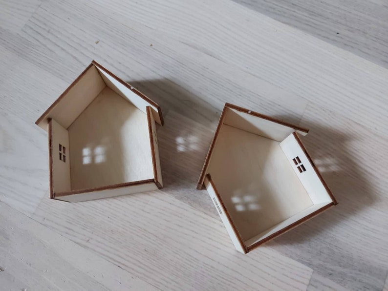 May include: Two unfinished wooden houses with cut-out windows. The houses are made of plywood and are sitting on a light wood surface.