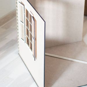 May include: A white dollhouse room with a window and shutters. The room is made of wood and has a light brown floor.
