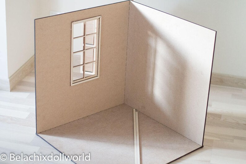 May include: A cardboard room with a single window, a light brown color, and a shadow on the wall. The room is empty except for two white sticks in the corner.