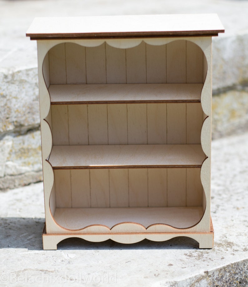 Pu&ograve; includere: Un piccolo scaffale in legno bianco con tre ripiani. I ripiani hanno un bordo a festoni e l'unit&agrave; ha un design semplice e rustico.