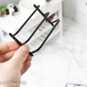 Może przedstawiać: Czarny metalowy stojak na ręczniki z trzema prętami. Stojak jest przeznaczony do łazienki w domku dla lalek.