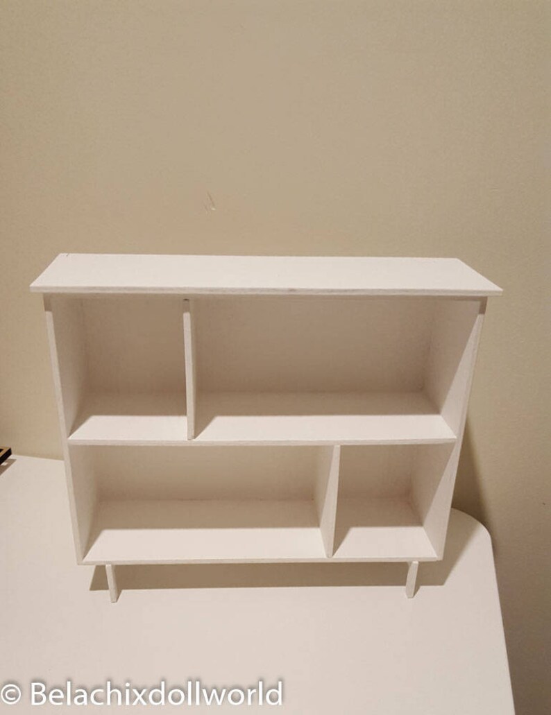 May include: White wooden shelf unit with five compartments. The shelf has a simple design and is perfect for displaying small items.