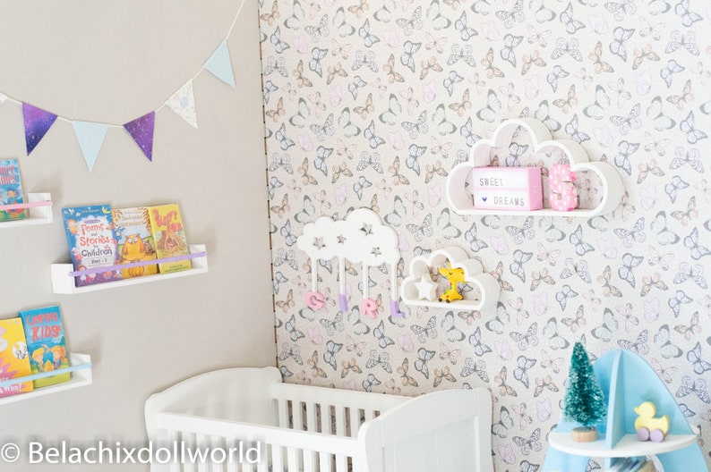 May include: A white crib with a white cloud-shaped shelf with the text "Sweet Dreams" and a pink number 5. The shelf is on a wall with a butterfly pattern wallpaper. There are also two other white cloud-shaped shelves with a star and a yellow giraffe toy.