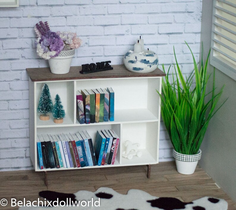 May include: White bookshelf with three shelves, filled with books and small potted plants. The bookshelf is against a white brick wall. The top shelf has a decorative bowl with candles and the word "Home" in black letters.
