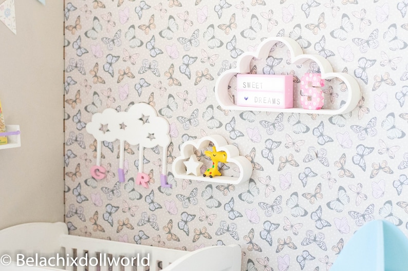 May include: White cloud-shaped shelves with a butterfly patterned wallpaper. The top shelf has a pink sign that says "Sweet Dreams" and a pink number "3". The bottom shelf has a yellow giraffe toy and a white star.