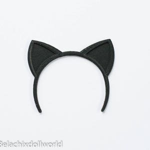 May include: Black cat ear headband. The headband features two upright, triangular cat ears. The ears and headband are a solid black color. The item is set against a white background. The text "Belachixdollworld" is at the bottom left.