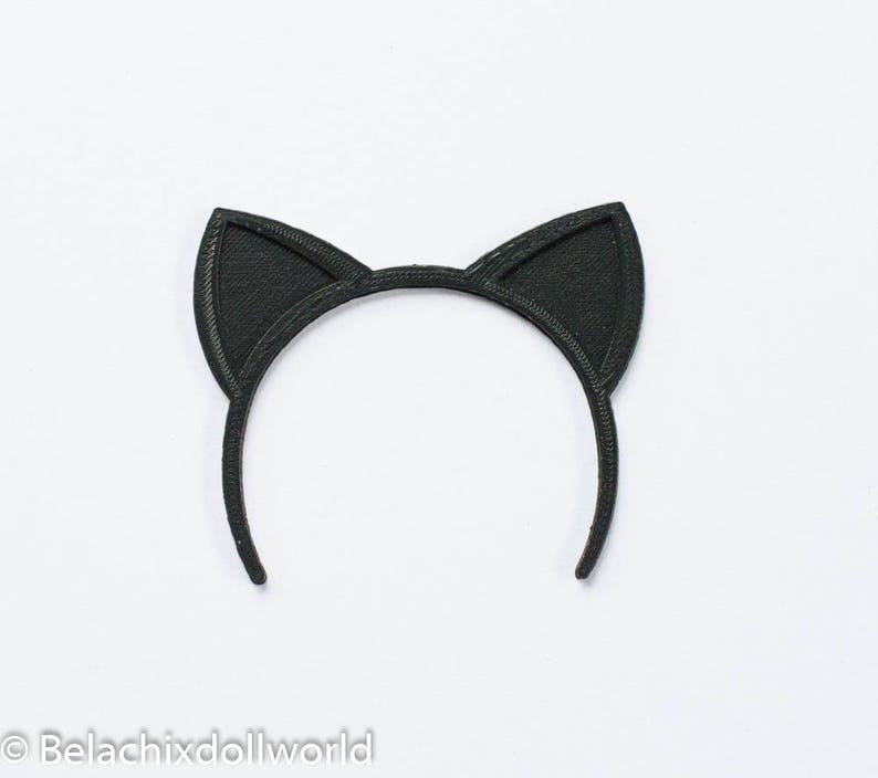 May include: Black cat ear headband. The headband features two upright, triangular cat ears. The ears and headband are a solid black color. The item is set against a white background. The text "Belachixdollworld" is at the bottom left.