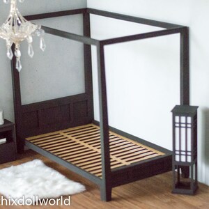 Puede incluir: Una cama con dosel negro con un colch&oacute;n de listones de madera y una alfombra blanca y esponjosa. Una peque&ntilde;a mesita de noche negra con una vela y un &aacute;rbol de Navidad en miniatura se encuentra junto a la cama. Una l&aacute;mpara de pie negra con una pantalla blanca se encuentra en la esquina.