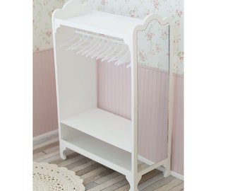 May include: White dollhouse furniture wardrobe with a shelf and a hanging rod. The wardrobe has a mirror on one side and a decorative top.