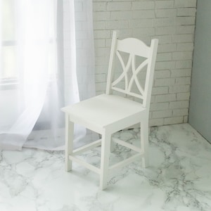 Peut inclure: Chaise en bois blanc avec un design simple, dot&eacute;e d'un dossier &agrave; lattes et d'une assise large. La chaise est pos&eacute;e sur un sol en marbre blanc.