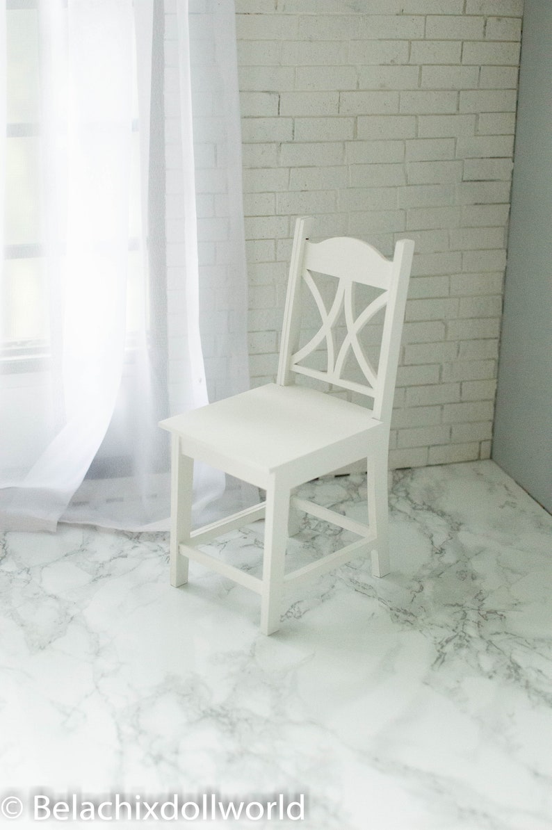 Peut inclure: Chaise en bois blanc avec un design simple, dot&eacute;e d'un dossier &agrave; lattes et d'une assise large. La chaise est pos&eacute;e sur un sol en marbre blanc.