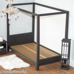 Puede incluir: Una cama con dosel negro con un colch&oacute;n de listones de madera y una alfombra blanca y esponjosa. Una peque&ntilde;a mesita de noche negra con un libro y una vela se encuentra junto a la cama. Una l&aacute;mpara de pie negra con una pantalla blanca se encuentra en la esquina.