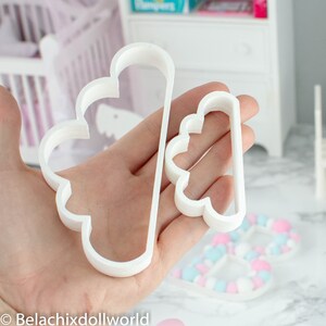 May include: Two white plastic cloud-shaped cookie cutters. The larger cutter is about 5 inches tall and the smaller cutter is about 3 inches tall.