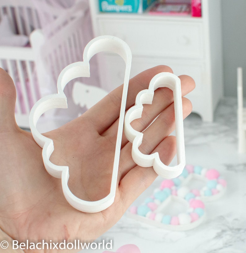 May include: Two white plastic cloud-shaped cookie cutters. The larger cutter is about 5 inches tall and the smaller cutter is about 3 inches tall.