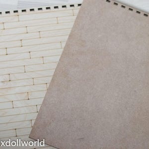 May include: A sheet of light brown craft paper with a woodgrain texture, placed on top of a sheet of white wood with a brick pattern.